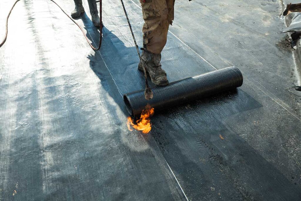 Workers sort old asphalt shingles, metal flashing, and roofing debris into separate covered containers.