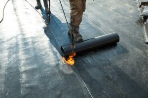 Workers sort old asphalt shingles, metal flashing, and roofing debris into separate covered containers.